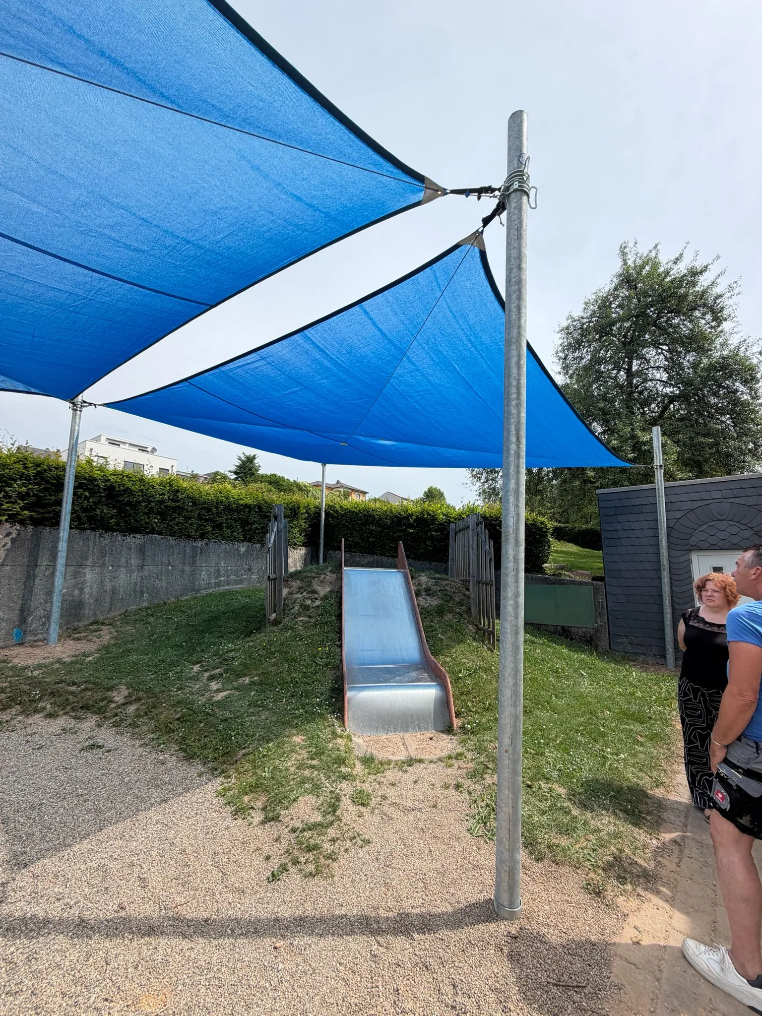 Sonnensegel über einer Edelstahlrutsche am Hang, montiert von Moshrif Spielplatzbau