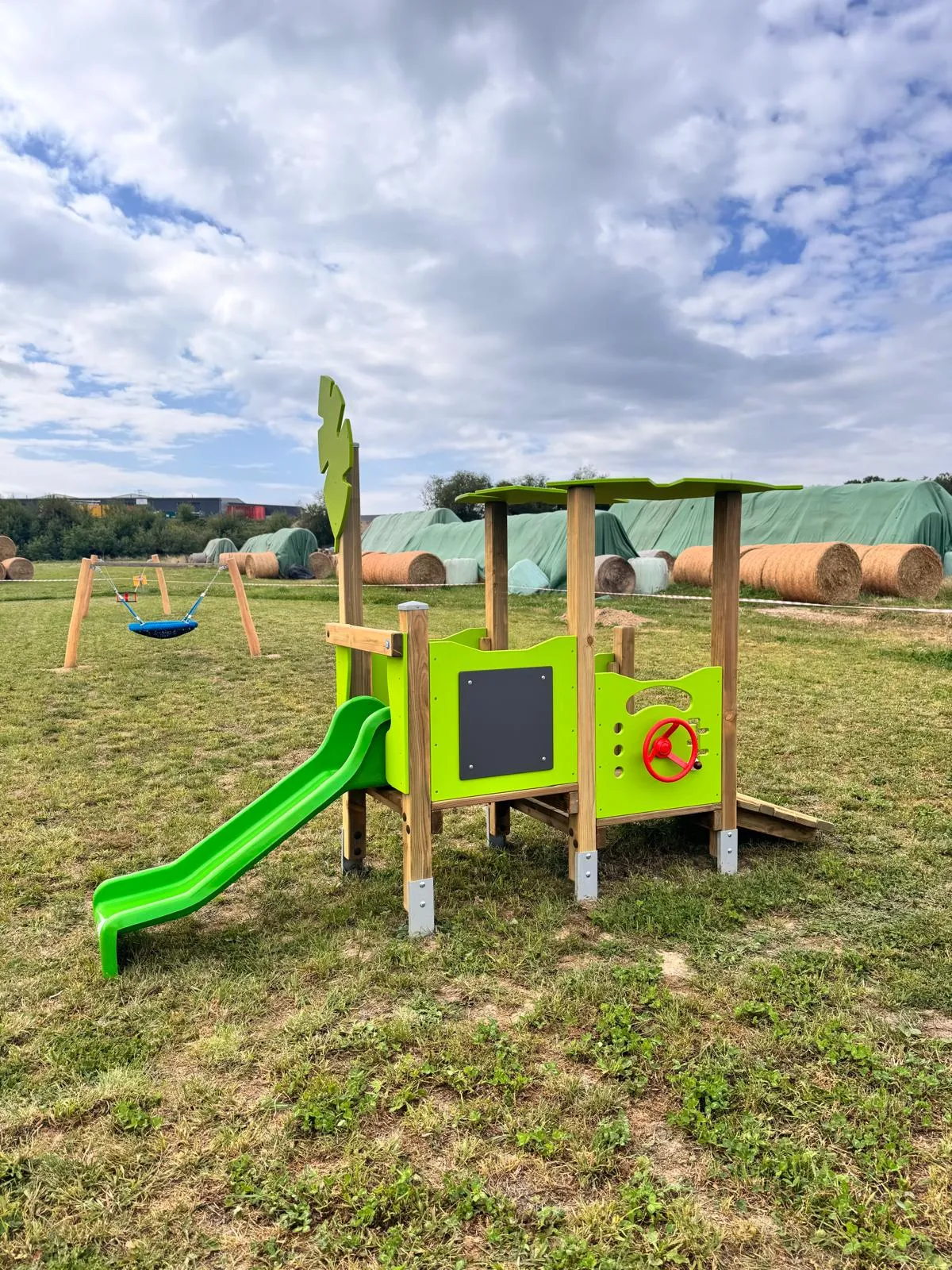 Themenspielgerät in Traktor-Form mit Rutsche auf einer Wiese, montiert von Moshrif Spielplatzbau in Augsburg