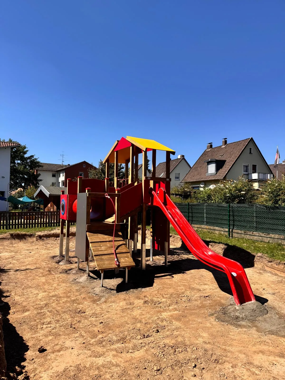 Spielturm mit rot-gelbem Dach und Rutsche im Sandbereich, montiert von Moshrif Spielplatzbau in Nürnberg